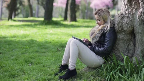 Pretty young  woman using tablet sitting under the tree Stock-Footage 75081098