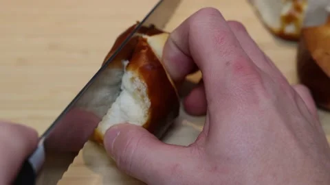 A pretzel bread is cut in half with a bread knife and made ready for a sandwich. 스톡 동영상 234544326