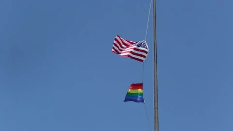 Pride flag is flailing in the wind with the flag of US, blue sky Stock Footage 155790484