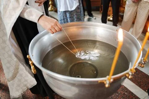 Priest hand lowering a cross on a string into holy water baptismal font Stock Photos