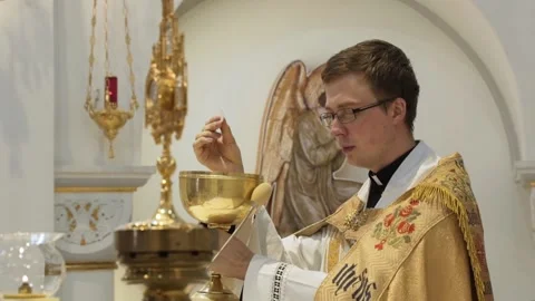 Priest holds God bread over bowl and reads prayer behind the altar. Stock Footage 169178985