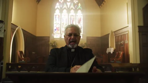 Priest talking in front of a window light Stock Footage 262292930