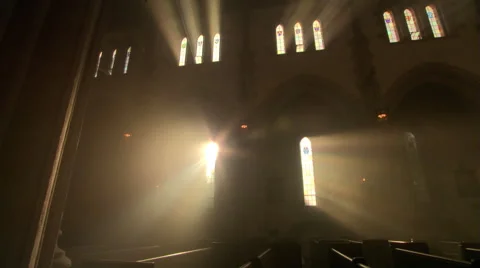 Priest walking down the aisle in darkened nave of Catholic church Stock Footage
