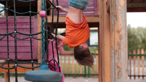 Primary school-age boy in an orange T-shirt hangs upside down in the playground. Stock Footage 144704080