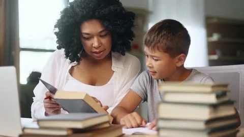 Primary school boy kid studying with his mother reading book at home Stock Footage 248689565