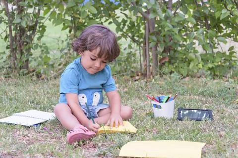 Primary school child lying on the grass doing homework. Stock Photos