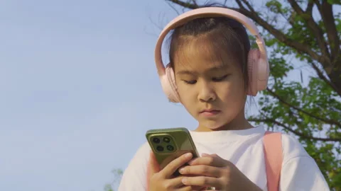Primary school girl using smartphone in the park, Digital learning concept. 库存影片 334271489