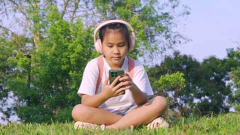 Primary school girl using smartphone in the park, Digital learning concept. 库存影片 334271550
