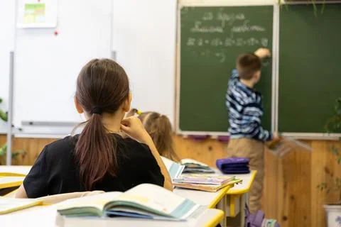 Primary school students learning in a classroom with a boy writing math equ.. Stock Photos