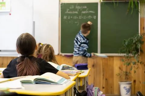 Primary school students sit at desks watching a classmate solve a math prob.. Stock Photos