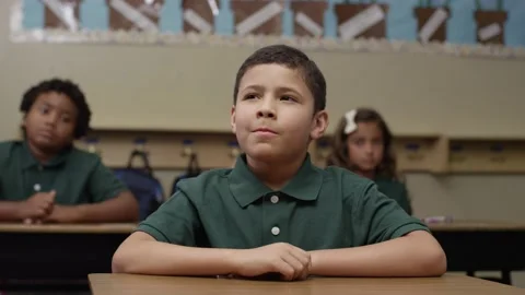 Primary students in uniforms sit in class as happy brown boy raises his hand Stock Footage 141757222