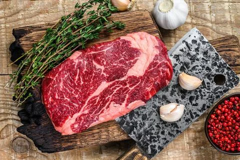 Prime rib eye raw beef meat steak on a butcher wooden cutting board with cleaver Stock Photos