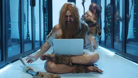 Primitive caveman of hunter-gatherers playing with laptop sitting on floor in Stock Footage 121123021