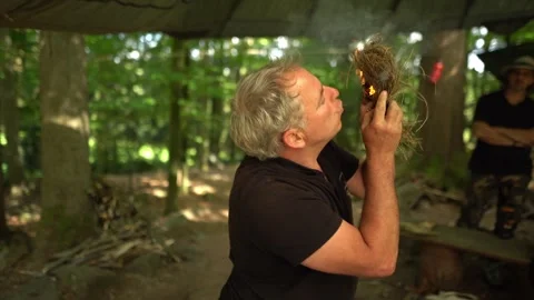 Primitive fire lighting demonstration as survival instructor blows into Видео 330970556