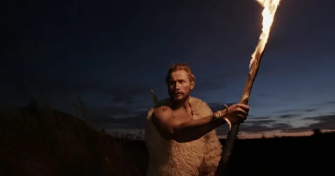 Primitive man wearing sheepskins using a torch taking a burning branch from a Video stock 140933652