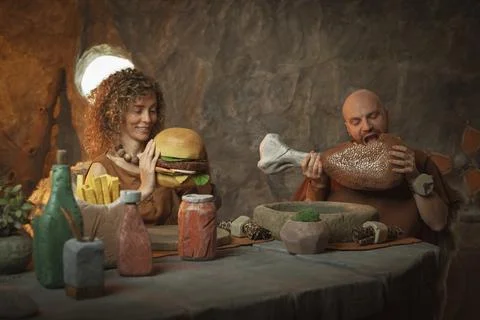 Primitive stone age couple having a delicious lunch in their cave Stock Photos