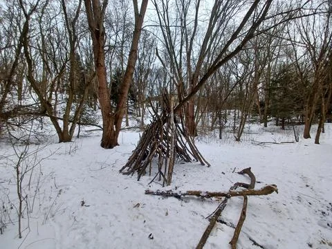Primitive teepee shelter made from branches in winter forest. Stock Photos