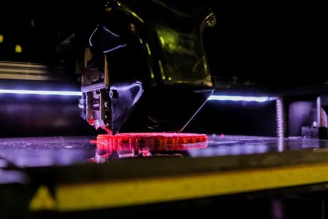 Print head of 3D printer machine printing red flat plastic model - close up Stock Photos
