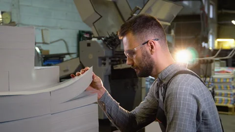 Print worker ready to place blank sheets of paper into offset machine for Stock Footage 257043709