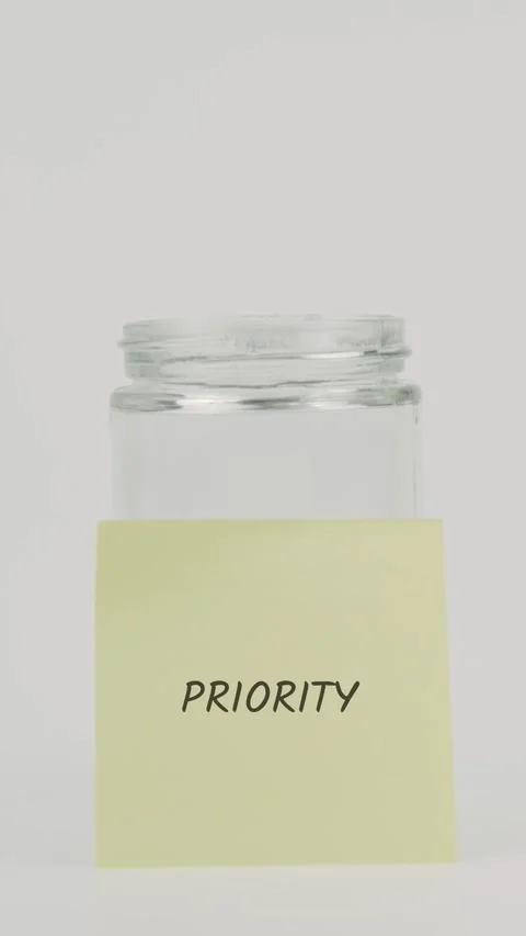 Priority text or word on yellow sticky note attached to glass jar with hand Stock Footage 311770408