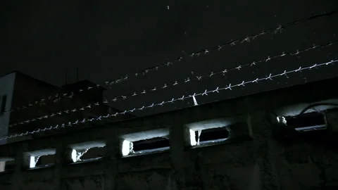 Prison barbed wire over concrete fence at cold dark winter night during snowfall Stock Footage 154599599