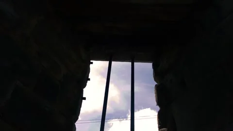 Prison bars on a stone wall silhouette against blue cloudy sky 스톡 동영상 338403677