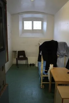 Prison Cell Interior With Barred Window, Bed, And Chair At Shrewsbury Prison Stock Photos