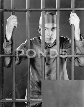 Prisoner behind bars looking angry and sad Stock Photos