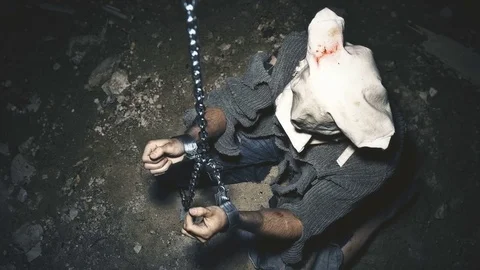 A prisoner in chains is closed in the basement where a little light penetrates Stock Footage 80238282