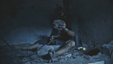 Prisoner in chains trying to cut the chain with a rock to escape Stock Footage 80065396