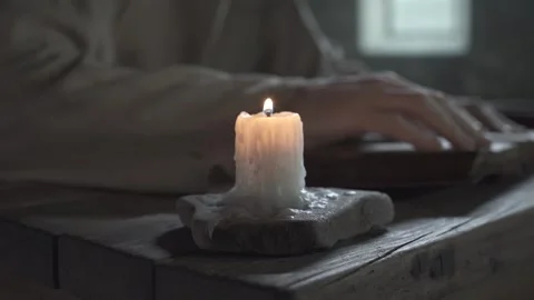 Prisoner hands tracing lines in a book near a candle, camera tracking Video stock 337648791