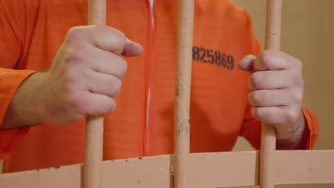 The prisoner in orange clothes holding bars of the prison cell with his his hand Stock Footage 167068430
