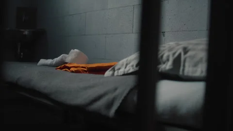 Prisoner puts orange uniform and bathroom accessories on the bed in prison cell 스톡 동영상 268561807