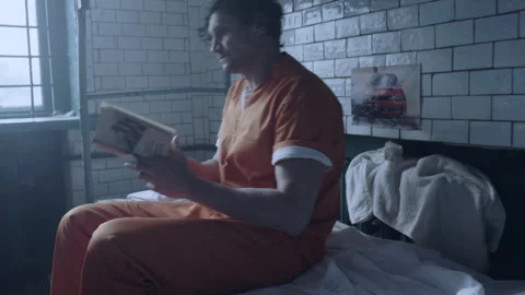 A prisoner reading a book in his cell with a car on the wall Stock Footage 283089675