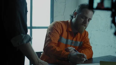 Prisoner signing for interrogator in a small dark room Stock Footage 275028069