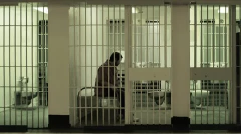 Prisoner sits on bed in cell, gets up and walks around Stock Footage 22792087
