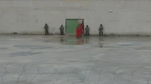 Prisoners in jumpsuits exiting a high security prison yard Stock Footage 330567046