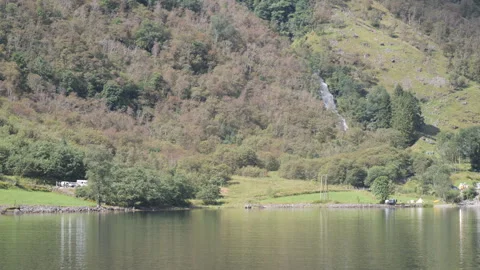 Pristine lake reflecting the green valleys and hills with a waterfall. Stock Footage 285685288