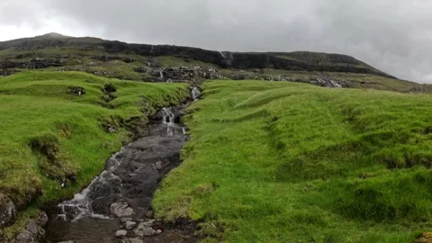 Pristine mountain stream flowing through green hills in Saksun, Faroe Islands Stock Footage 339383280