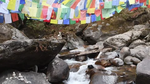 Pristine river flowing down with fluttering prayer flags above Stock Footage 268950344
