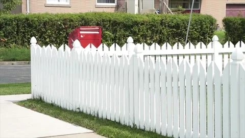 Pristine white picket fence with red mailbox and road bush behind Stock Footage 248711610
