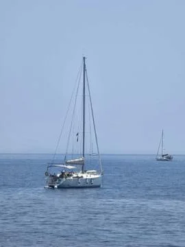 A pristine white sailboat without raised sails floats on a vast expanse of calm Stock Photos