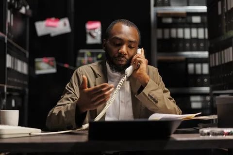 Private detective explaining evidence to client on landline phone Fotos Stock