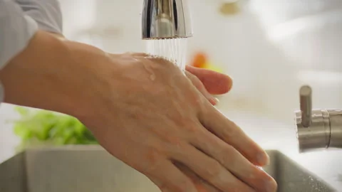 In private kitchen young man carefully washes his hands under running tap. H Stock Footage 281374928