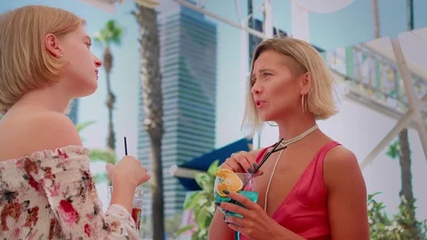 Private talk of two young Caucasian females with blue cocktails standing at Stock Footage 119385676