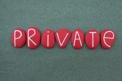 Private text composed with handmade red colored stone letters over green sand Stock Photos