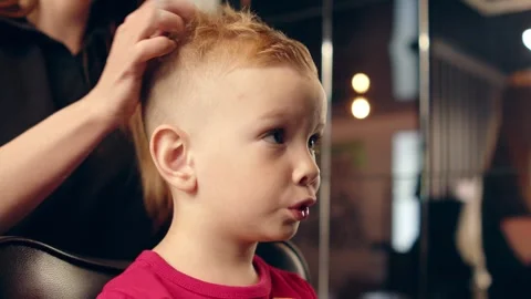Pro barber styling a small boy's hair in a modern barbershop with wax. Stock Footage 335504815