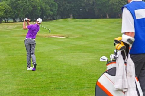 Pro golfer playing a shot with caddy Stock Photos