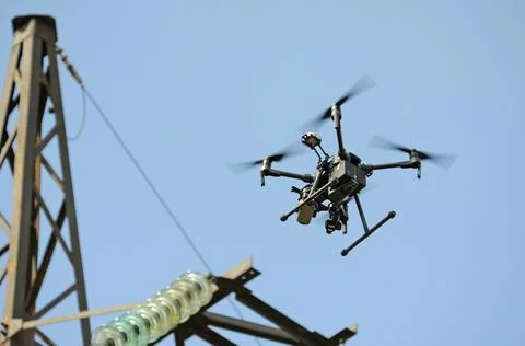 Pro quadcopter with camera aboard flying in a sky, electric pylon, cables and Stock Photos