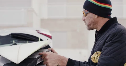 Pro surfer David Langer adjusting surfing gear on top of vehicle on windy day Stock Footage 164314246